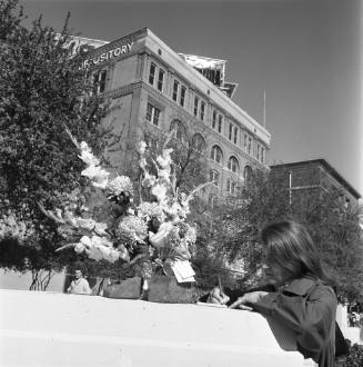 Image of a woman writing a note next to a flower arrangement in Dealey Plaza