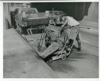 Photograph of a man removing a section of curb from Main Street in Dealey Plaza
