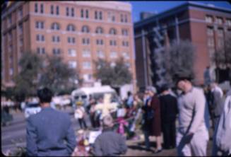 Image of the Texas School Book Depository building and mourners in Dealey Plaza