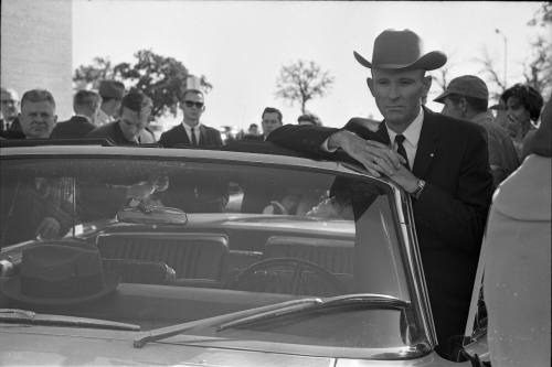 Image of people listening to a car radio for news outside of Parkland Hospital