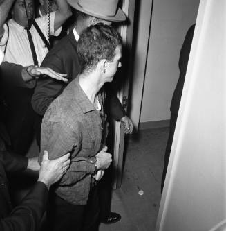 Image of Lee Harvey Oswald in handcuffs at the Dallas Police Department