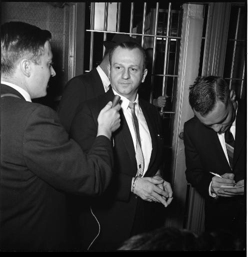 Image of Jack Ruby in handcuffs escorted by police, answering questions