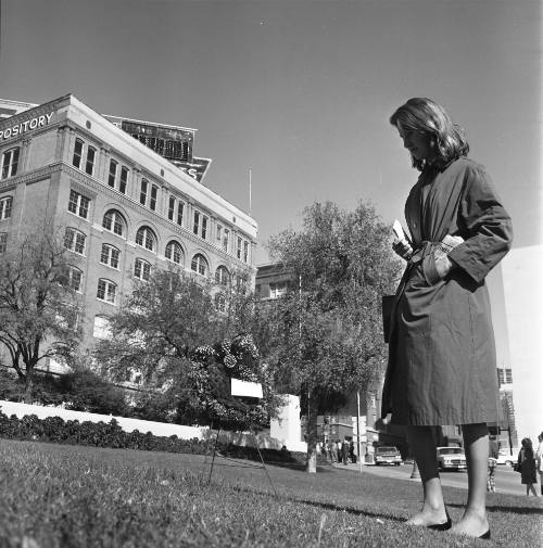 Image shows a woman on the grassy knoll looking at a memorial wreath