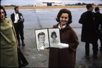 Image of Maria Anagonstou at Love Field holding drawings of the Kennedys