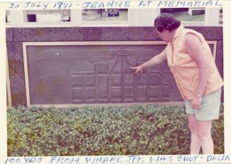 Color photo of Jeanne Reilly pointing to a historical marker in Dealey Plaza