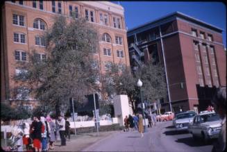 Image of the Texas School Book Depository building and mourners in Dealey Plaza